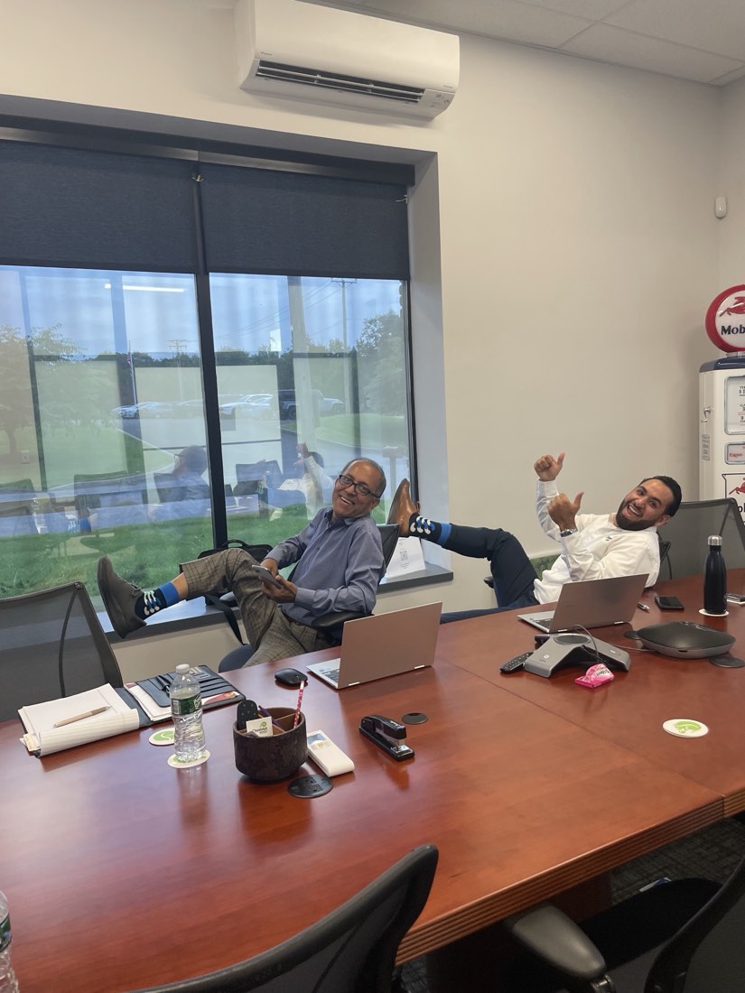 Two coworkers laughing in a conference room with their feet up on the table and thumbs up, socks on display