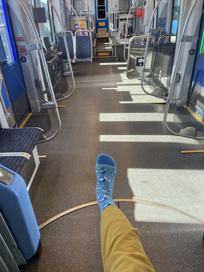 A foot in a blue Rovertown sock and no shoe, stretched out across the floor of a nearly empty light rail car