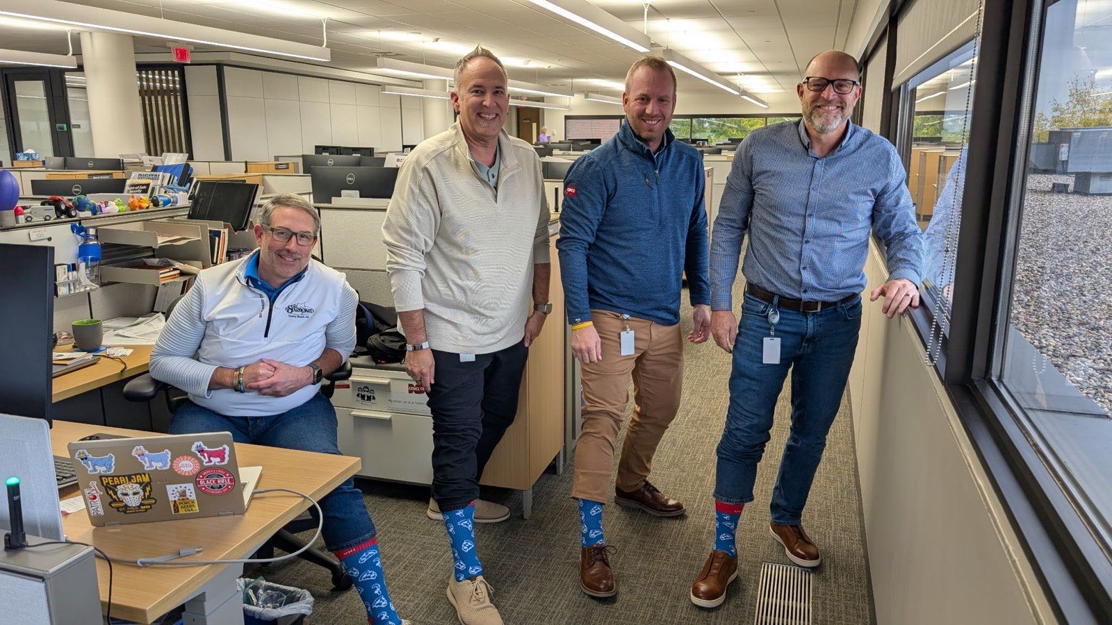 Four coworkers in the office with trousers rolled up to show off their blue Rovertown socks