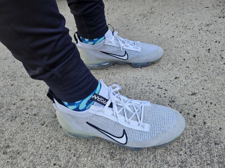 White Nike VaporMax sneakers and black joggers on a concrete sidewalk, with blue and green camouflage-pattern Rovertown socks showing at the ankle